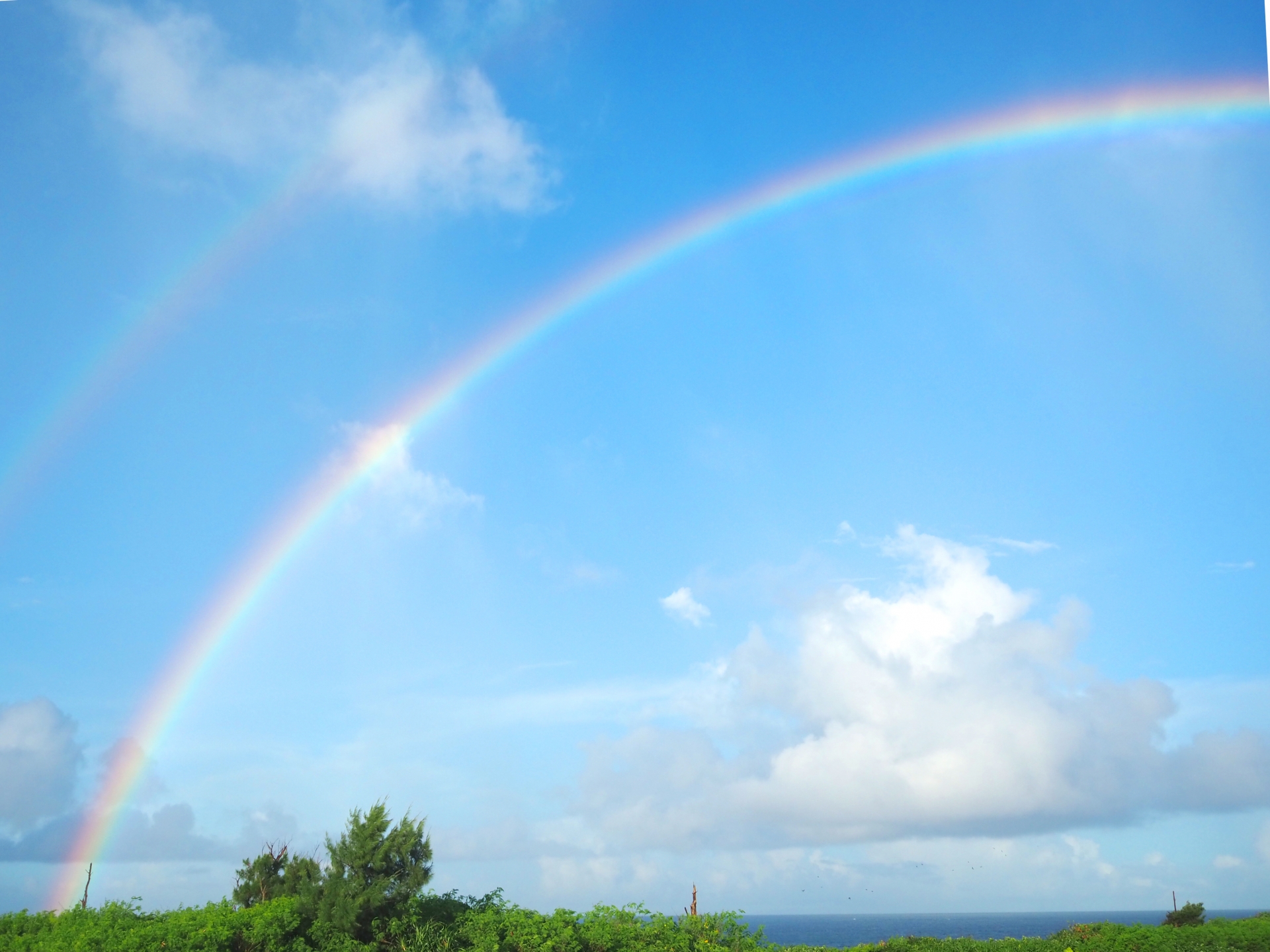 青空にかかる二重の虹。幸運や希望、前向きな朝のエネルギーを象徴するイメージ