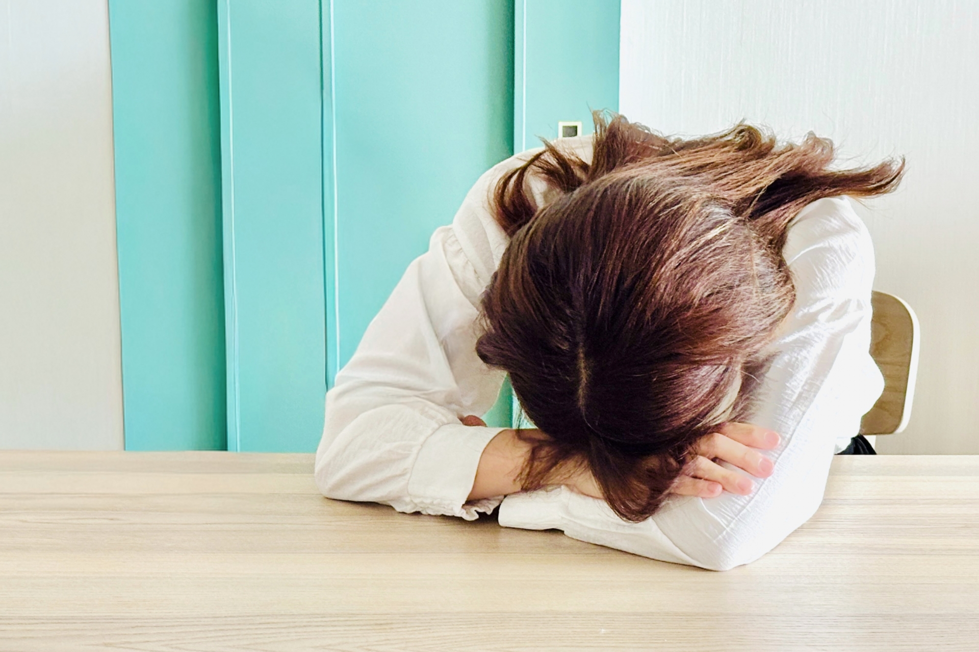 机にうつ伏せて休む女性。疲れを感じながら心と体をリセットするイメージ